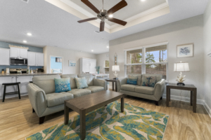 Spacious coastal-themed living room at Beach Bliss vacation rental in Panama City Beach, featuring comfortable sofas, a ceiling fan, and large windows.