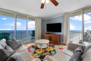 A brightly lit living and dining area inside a luxury beachfront condo rental at Tidewater Beach Resort in Panama City Beach, featuring comfortable seating, a flat-screen TV, and large sliding glass doors opening to a Gulf-front balcony.
