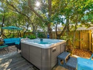 An outdoor luxury hot tub built into a wooden deck at dusk, surrounded by tropical landscaping at Barefoot Paradise vacation rental home in Panama City Beach, Florida.
