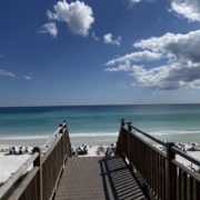 Wooden beach boardwalk leading down to the white sand and emerald water under a blue sky with dramatic clouds in Panama City Beach, Florida.