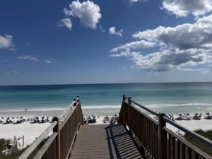 Wooden beach boardwalk leading down to the white sand and emerald water under a blue sky with dramatic clouds in Panama City Beach, Florida.