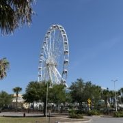pcb-wheel-ferris-wheel-pier-park-panama-city-beach A high-angle view of the massive 200-foot PCB Wheel at Pier Park in Panama City Beach, featuring its fully enclosed, climate-controlled gondolas against a bright blue Florida sky.