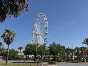 A high-angle view of the massive 200-foot PCB Wheel at Pier Park in Panama City Beach, featuring its fully enclosed, climate-controlled gondolas against a bright blue Florida sky.