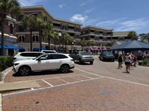 A vibrant palm-lined walkable street scene in front of Seacrest Beach on 30A, featuring upscale shops, parked cars, and beautiful coastal architecture under a clear sky.