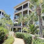 Luxury multi-story beach house with palm trees and a paved walkway in Panama City Beach