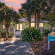 Exterior view of Barefoot Paradise, a pet-friendly vacation rental house in Panama City Beach, Florida, featuring a charming coastal design, private driveway, and lush landscaping under a dusk sky.
