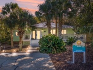 Exterior view of Barefoot Paradise, a pet-friendly vacation rental house in Panama City Beach, Florida, featuring a charming coastal design, private driveway, and lush landscaping under a dusk sky.