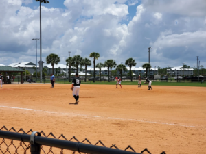A youth baseball game in progress under a bright blue sky at Frank Brown Park's premier sports complex in Panama City Beach, Florida.