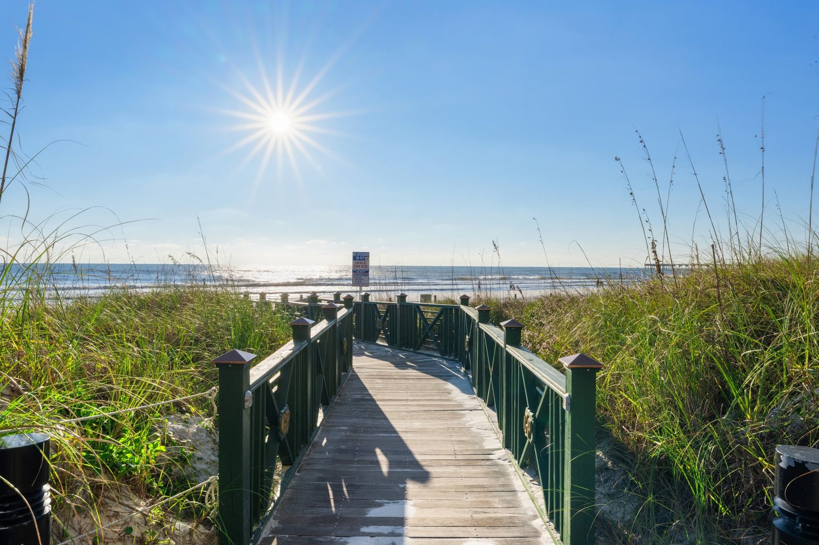 Wooden boardwalk with railings leading over the dunes and sea oats to the beach