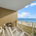 Gulf-front condo balcony with white Adirondack chairs and a grill, overlooking the dunes and beach