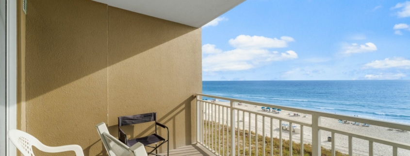 Gulf-front condo balcony with white Adirondack chairs and a grill, overlooking the dunes and beach
