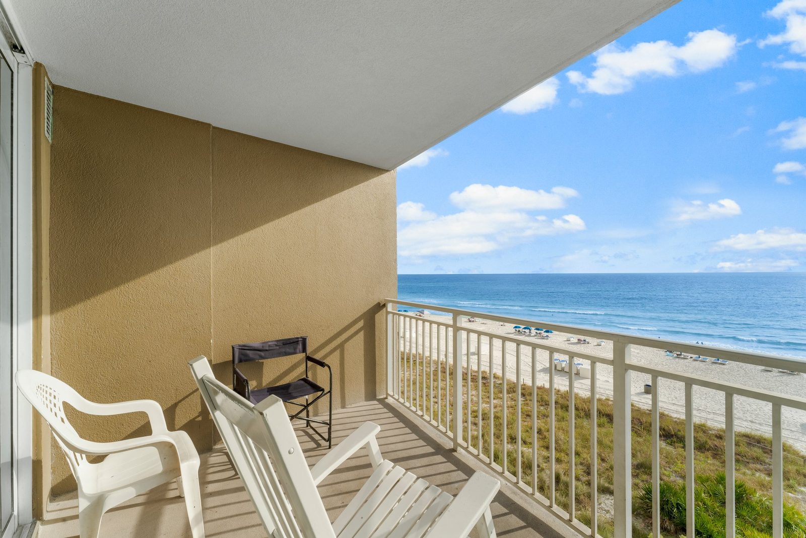 Gulf-front condo balcony with white Adirondack chairs and a grill, overlooking the dunes and beach