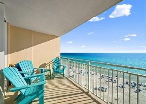 Two teal Adirondack chairs on a private balcony looking out over the emerald ocean and beach in Panama City Beach