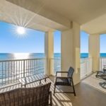 Covered condo balcony with two chairs and a table, looking out over the Gulf at sunrise
