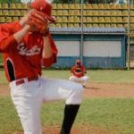 A youth baseball player pitching the ball on a turf field during a tournament.
