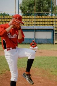 A youth baseball player pitching the ball on a turf field during a tournament.